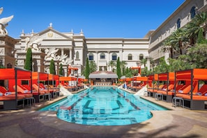 A swimming pool with lounge chairs, a grand building with statues, and palm trees.