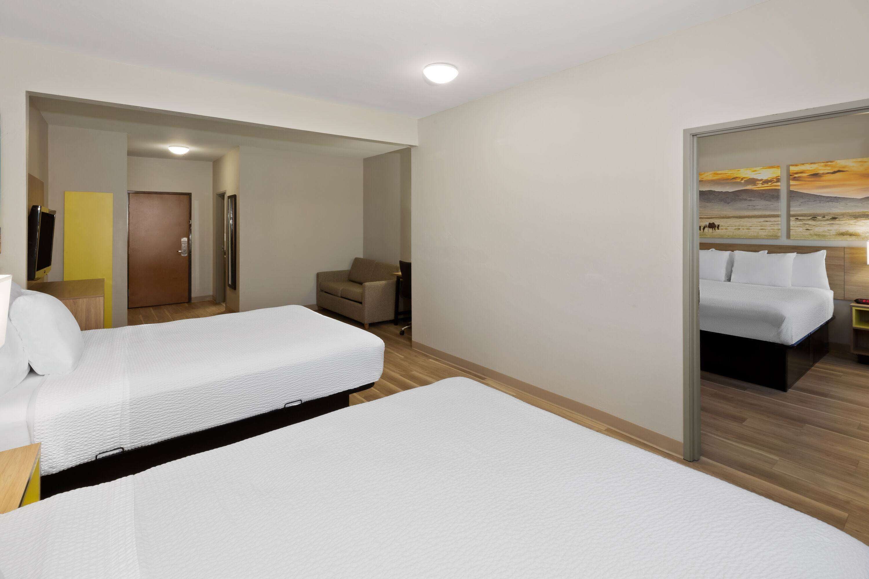 A hotel room with two beds, a wooden floor, a door, a small table, and a wall with a painting.