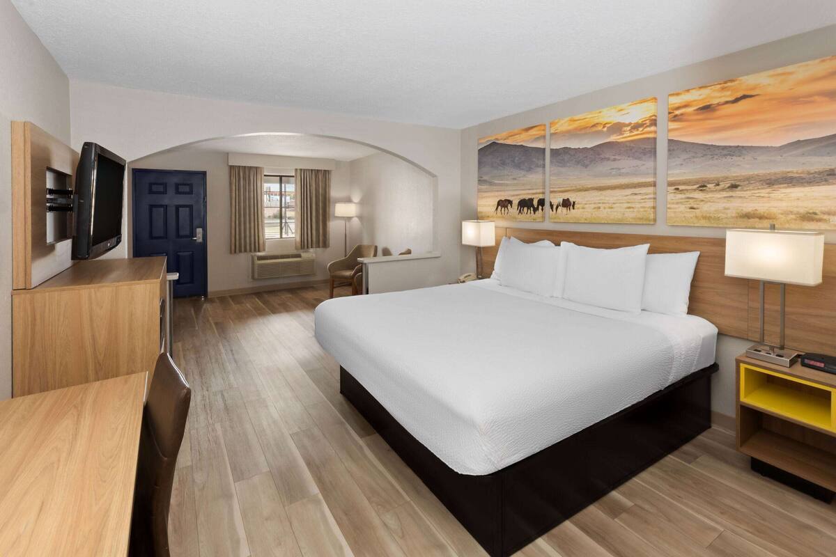 Une chambre d’hôtel moderne avec un grand lit, un bureau, une télévision et un tableau représentant un paysage.