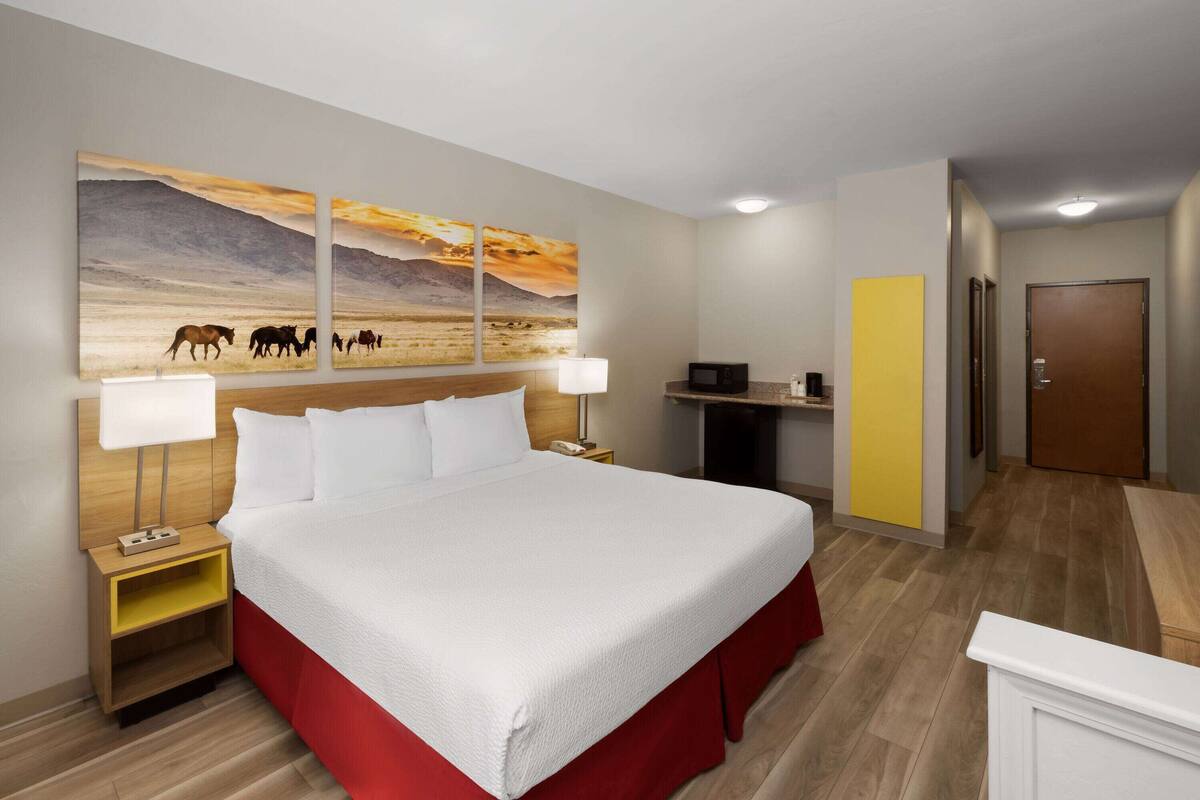 Une chambre d’hôtel avec un grand lit, une table de chevet avec une lampe, une petite table avec un téléphone et un tableau représentant des chevaux accroché au mur.