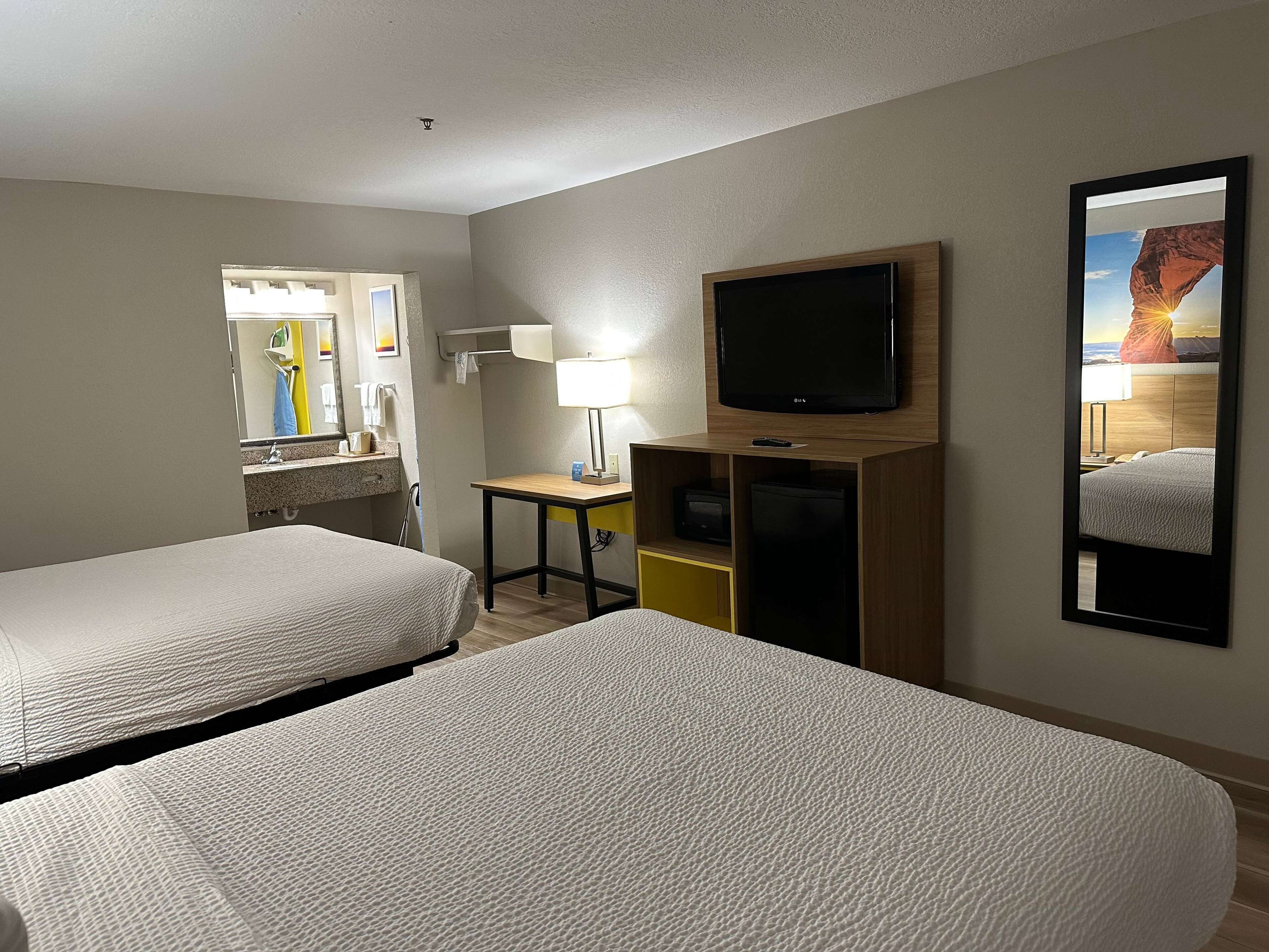 A hotel room with two beds, a TV, a desk with a lamp, a mirror, and a view of a canyon.