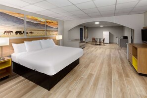 Quarto de hotel com uma cama grande, uma escrivaninha, uma cadeira, uma televisão e um quadro na parede.