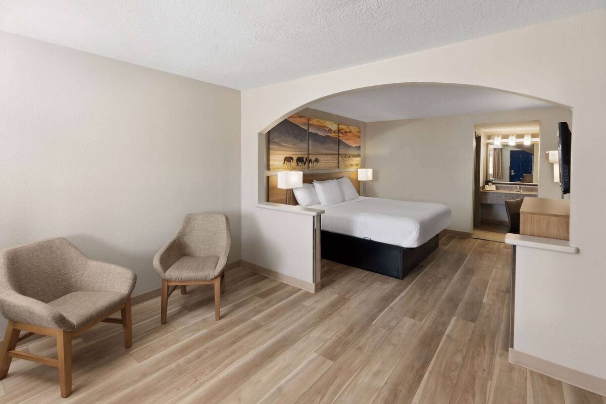 Une chambre d’hôtel avec un lit, deux chaises, un bureau, un miroir et un tableau au mur.