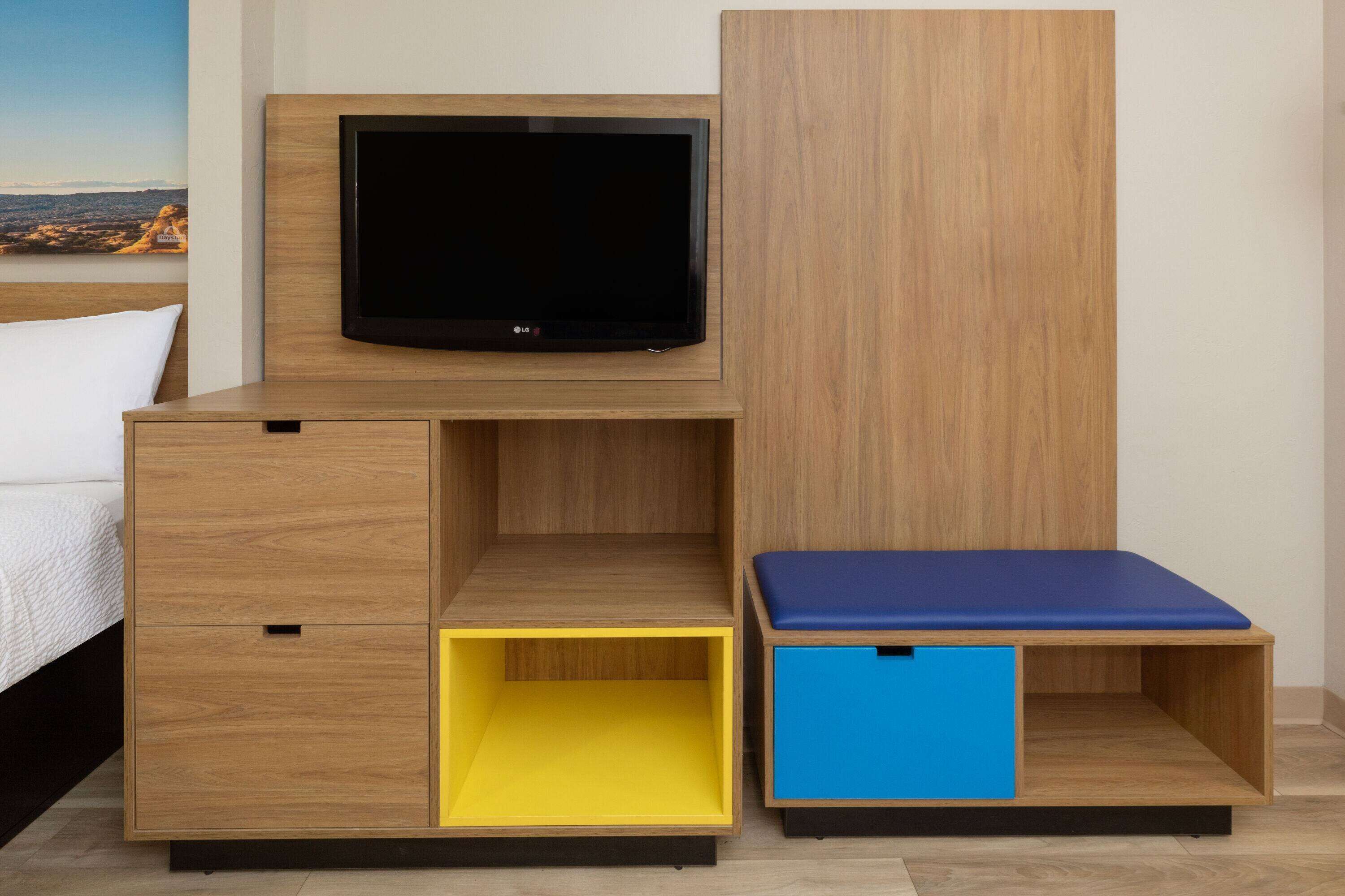 A modern room with a bed, a TV mounted on a wooden cabinet, and a small blue bench.