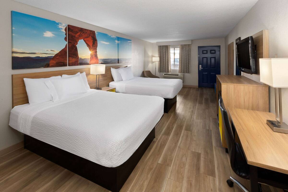 Une chambre d’hôtel avec deux lits, un bureau, une télévision et un tableau représentant un paysage.