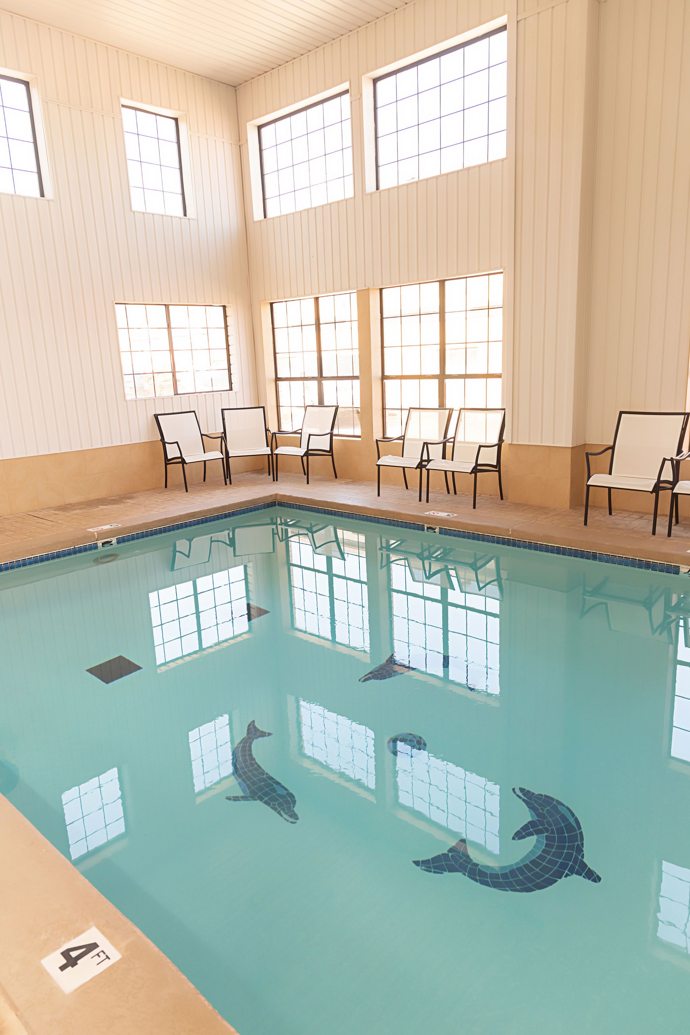Una piscina interna con acqua cristallina, pareti piastrellate e numerose finestre.