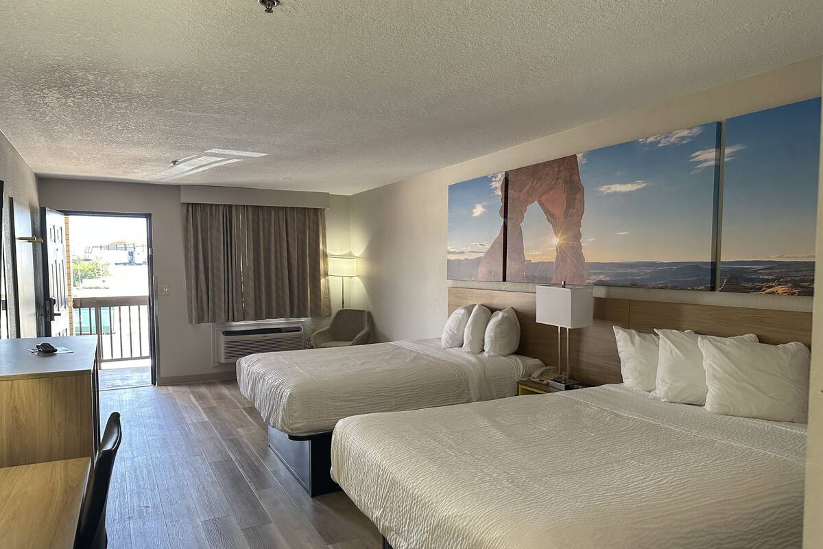 Une chambre d’hôtel avec deux lits, un bureau, une chaise, une lampe et une grande fenêtre donnant sur la montagne.
