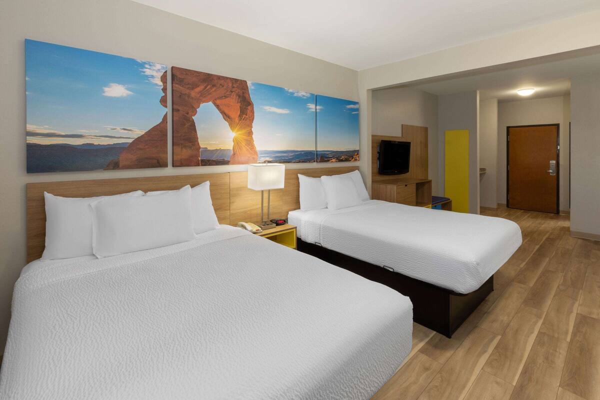 Une chambre d’hôtel avec deux lits, une grande fenêtre donnant sur le coucher de soleil, un téléviseur à écran plat et un plancher en bois.