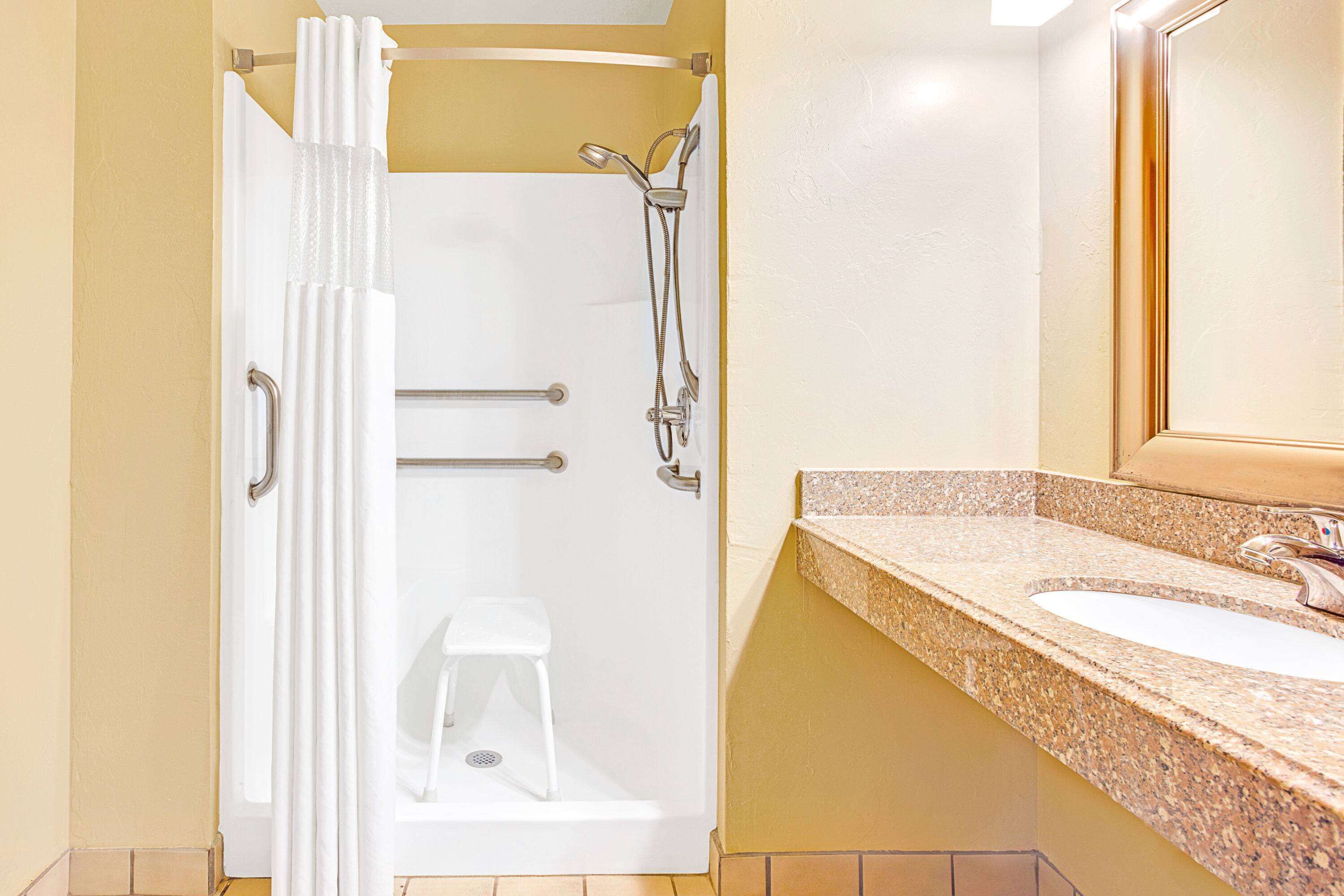 Een badkamer met douche, handgrepen, een wastafel en een spiegel.