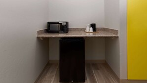 Een kleine kitchenette met een magnetron, koffiezetapparaat en een vuilnisbak.