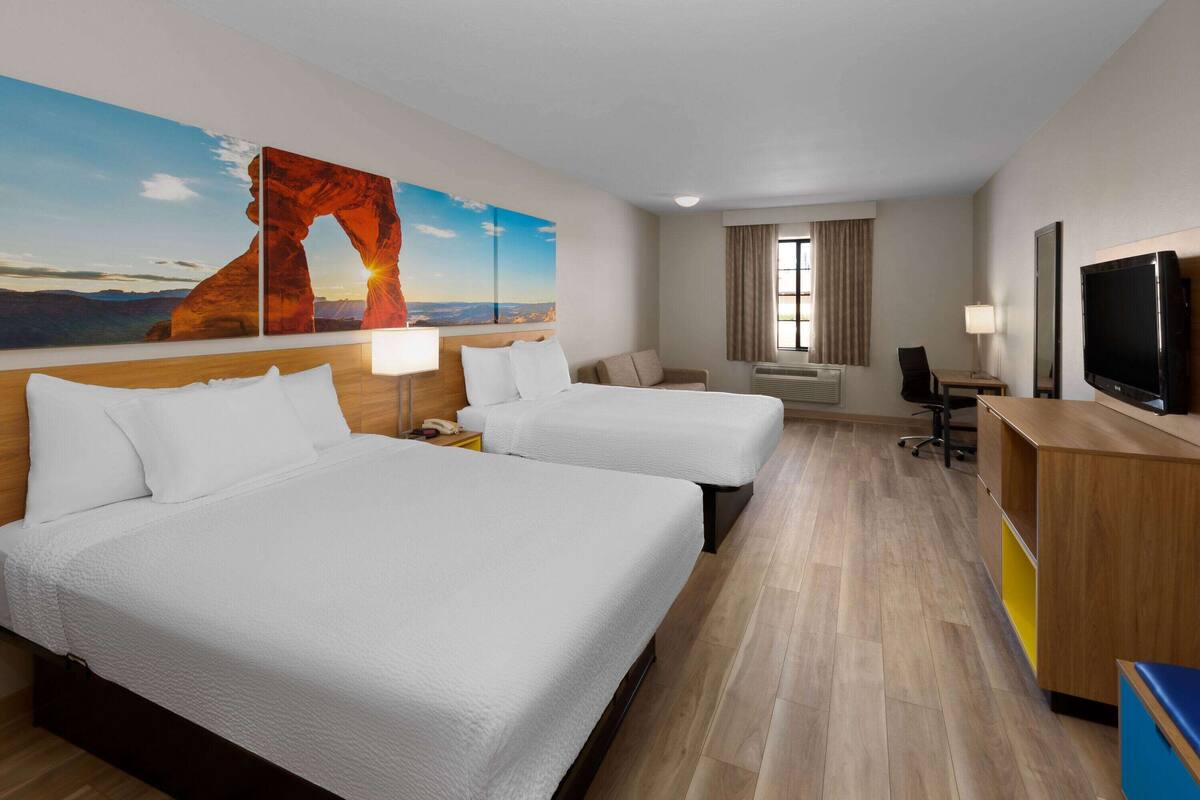 Une chambre d’hôtel avec deux lits, un bureau, une télévision et un grand tableau représentant une formation rocheuse.