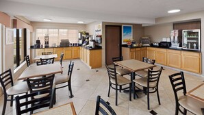 Een restaurantgedeelte in een hotel met meerdere tafels en stoelen, een keuken met apparatuur, en uitzicht op het buiten.