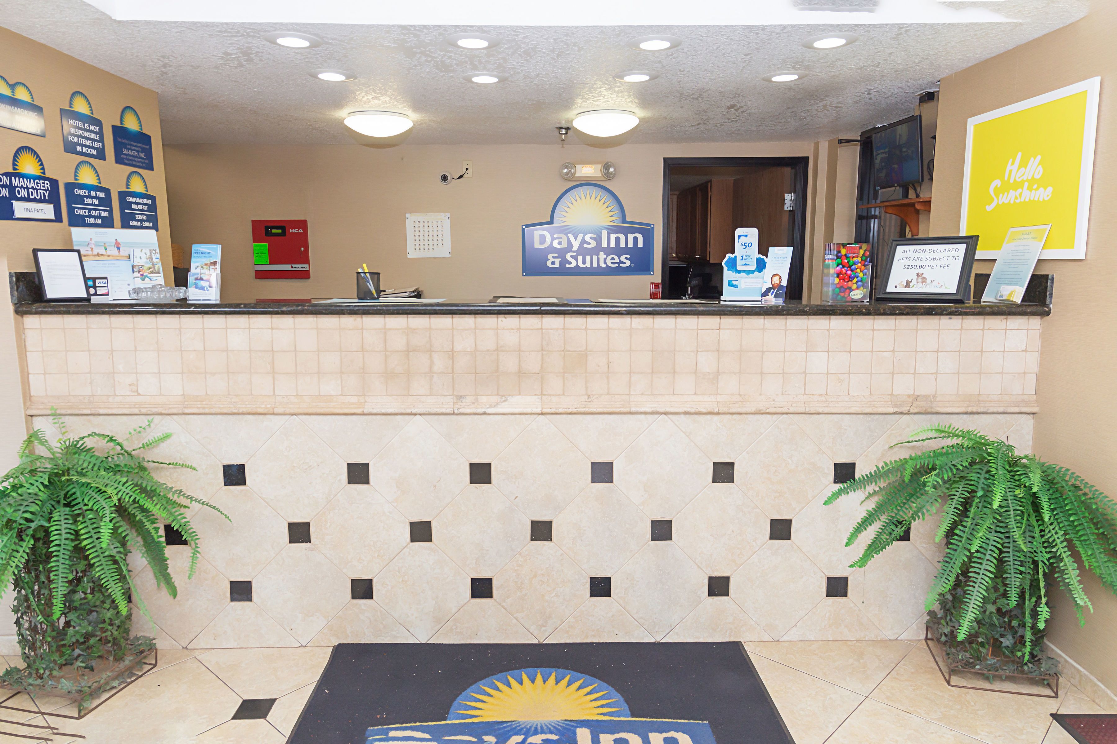 Un espace d’accueil avec une enseigne « Days Inn & Suites », un mur recouvert de carreaux et deux plantes en pot.