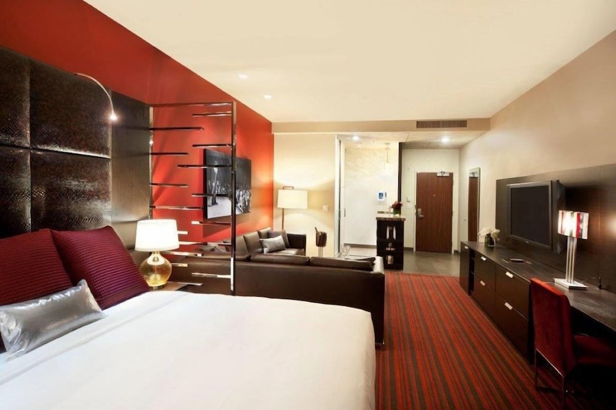 Une chambre d’hôtel avec un grand lit, un bureau, une télévision et une moquette rouge.