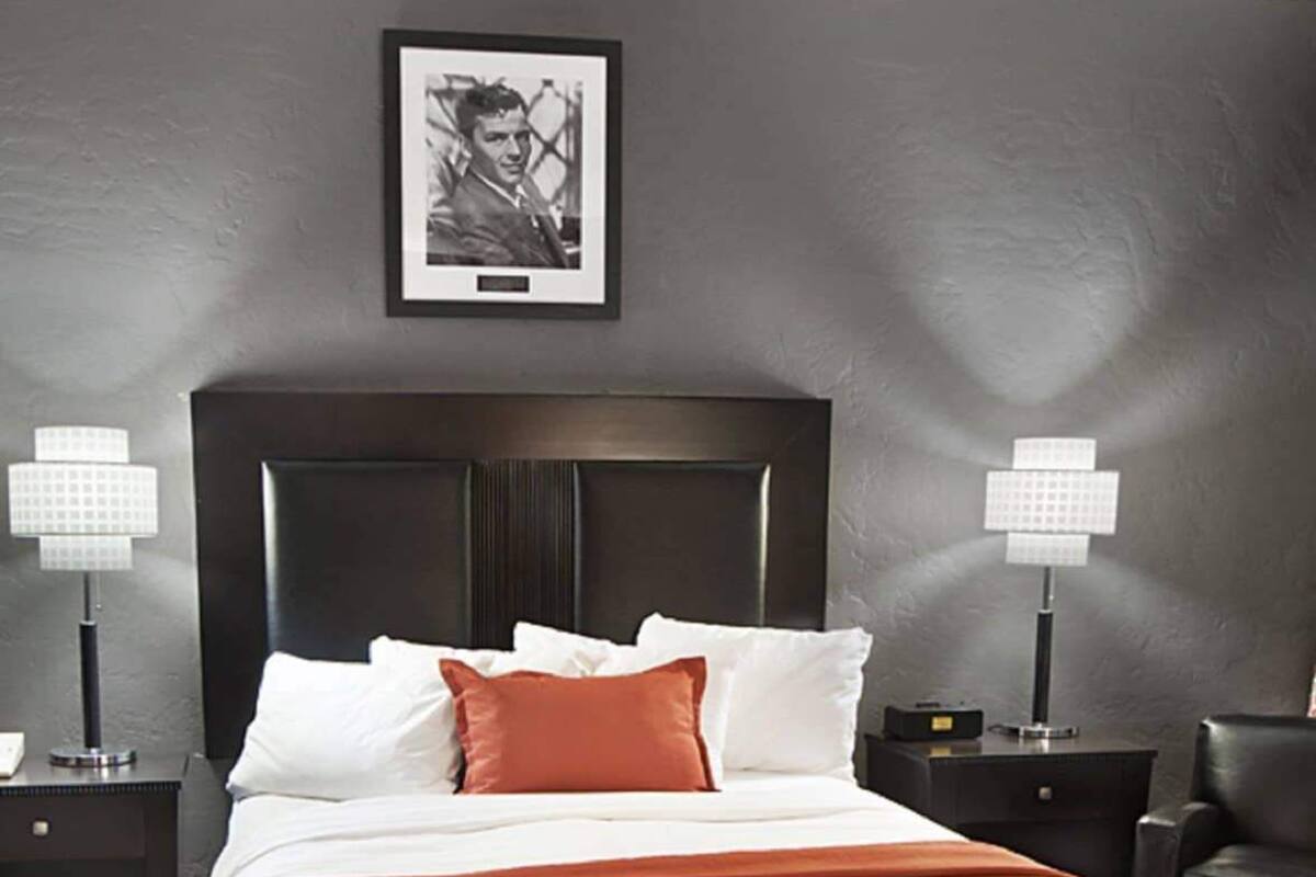 Una cama bien hecha con ropa de cama blanca y naranja, un cabecero oscuro y dos lámparas de noche.