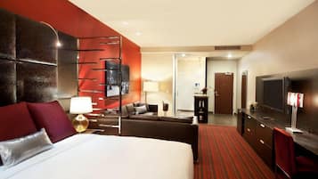 Habitación de hotel con una cama grande, un escritorio, un televisor y una pared de acento roja.