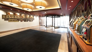 Un hall d’hôtel avec un grand tapis noir, un mur orné d’une enseigne « GOLDEN GATE », et une rangée de vieux jeux d’arcade.