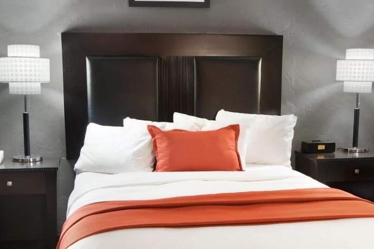 Una cama bien hecha con ropa de cama blanca y naranja, dos lámparas de noche y un cabecero oscuro.