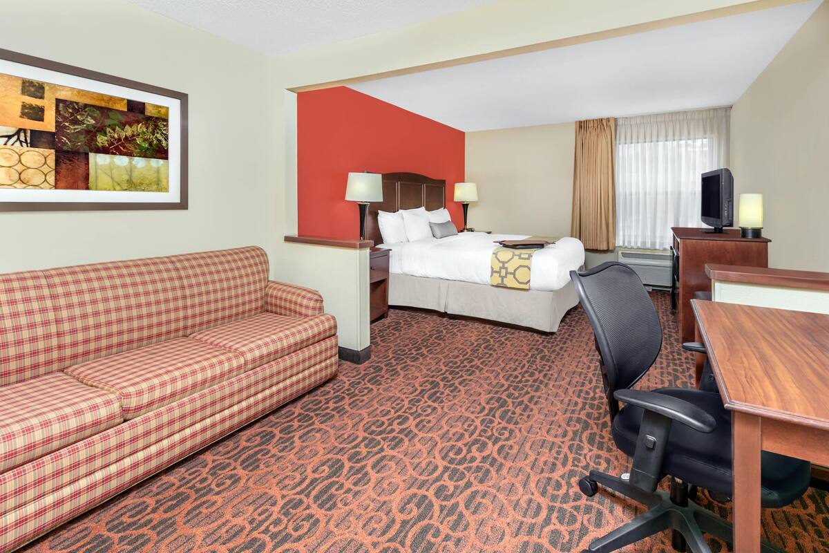 Une chambre d’hôtel avec un lit, un canapé rouge, un bureau avec une chaise, une télévision et un tableau accroché au mur.