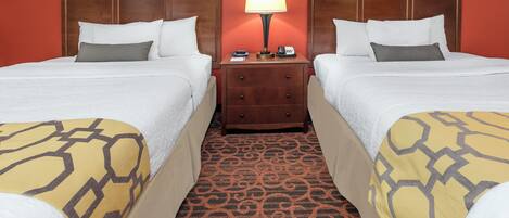 A hotel room with two beds, a nightstand with a lamp, and a patterned carpet.