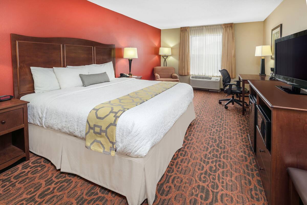 Une chambre d’hôtel avec un grand lit, un bureau avec une télévision, une chaise, une lampe de bureau et une fenêtre avec des rideaux.