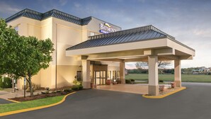 A Baymont Inn with a covered entrance, a parking lot, and a landscaped area with trees. - Baymont by Wyndham Oklahoma City/Quail Springs (Oklahoma City)