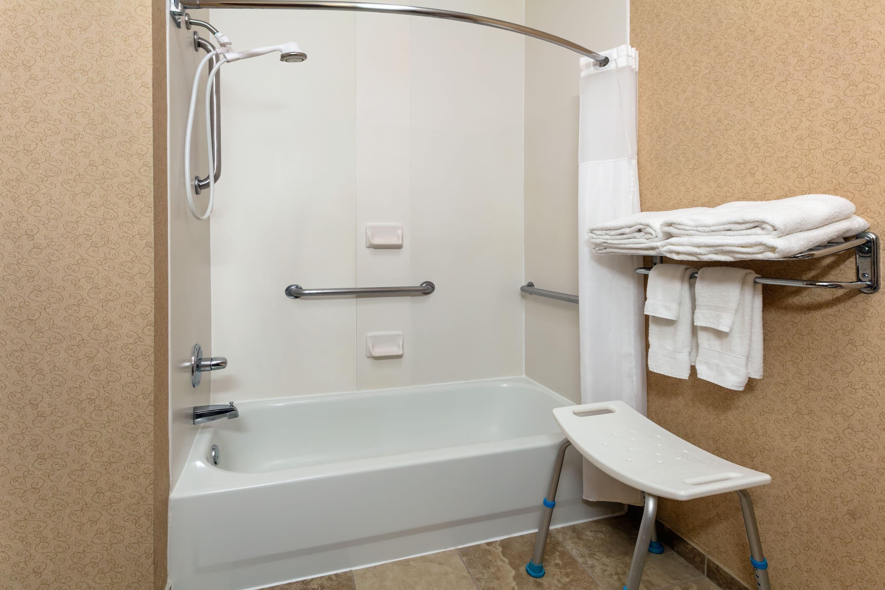 Une douche équipée d’une barre d’appui, une baignoire blanche et un petit marchepied.