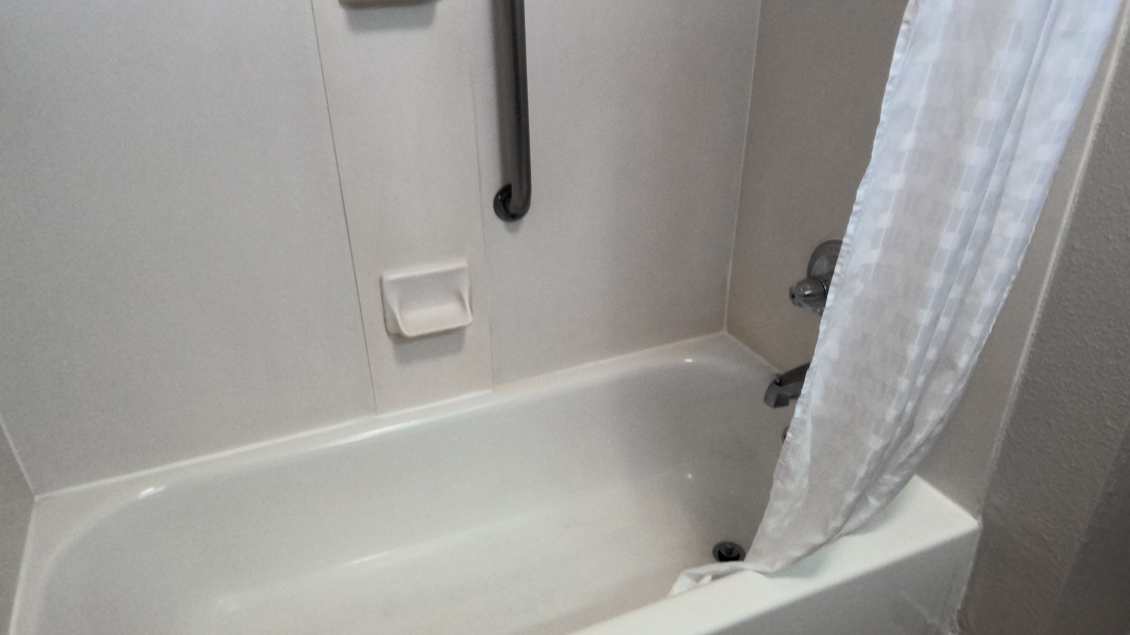 A white bathtub with a shower curtain, a handheld showerhead, and a small control panel.