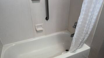 Una bañera blanca con cortina de ducha, cabezal de ducha manual y un pequeño panel de control.