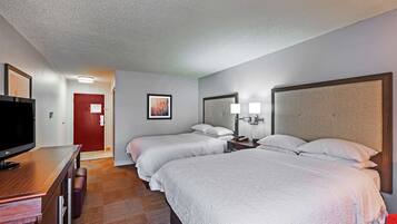 A hotel room with two beds, a desk with a flat-screen TV, a red door, and a framed picture on the wall.