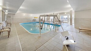 Une piscine intérieure dotée d’un plongeoir, de chaises longues et d’un sol carrelé.