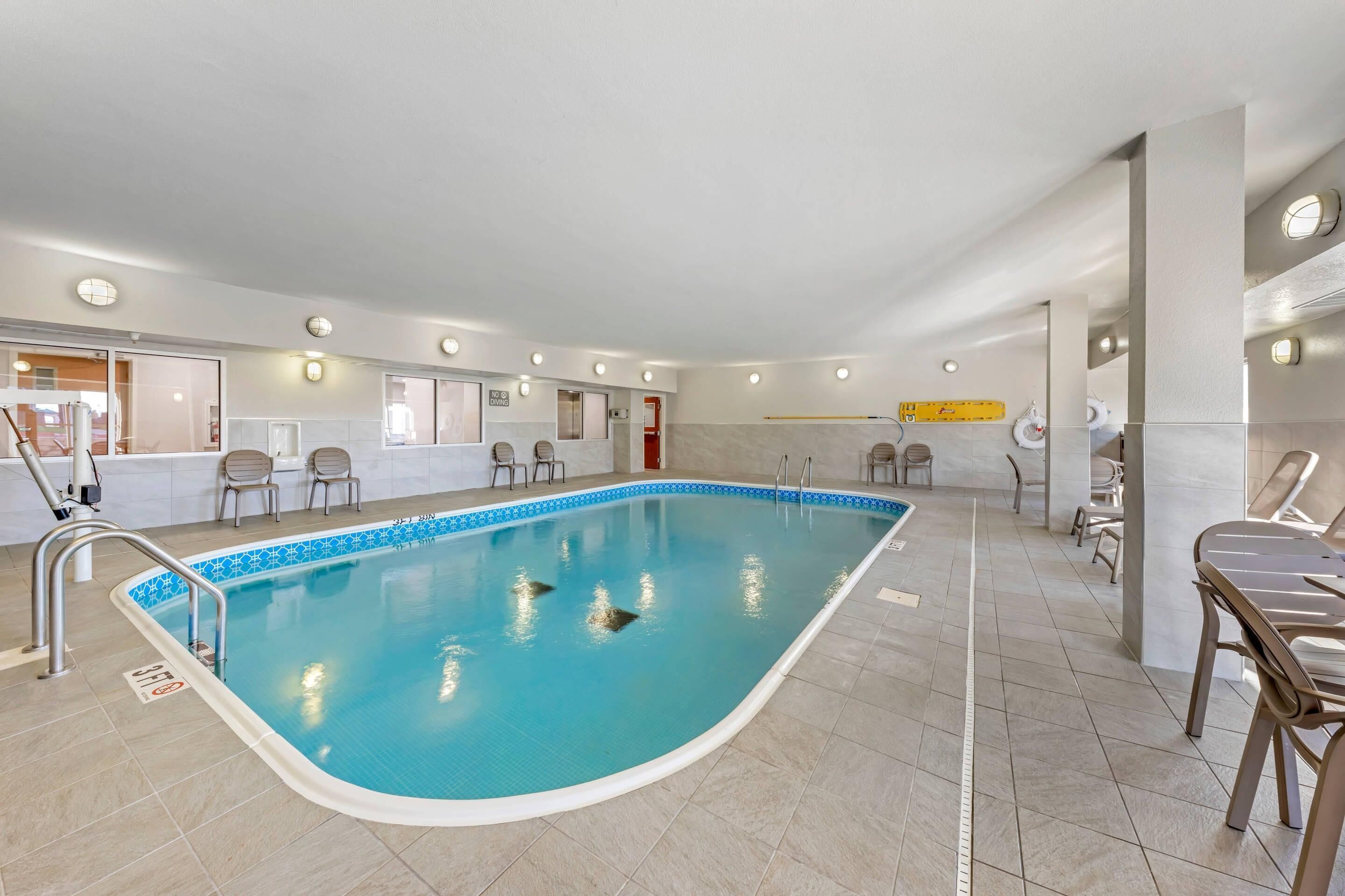 Una piscina interior con agua cristalina, rodeada de suelo de baldosas y equipada con sillas junto a la piscina.