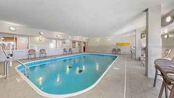 Una piscina interior con agua cristalina, rodeada de suelo de baldosas y equipada con sillas junto a la piscina.
