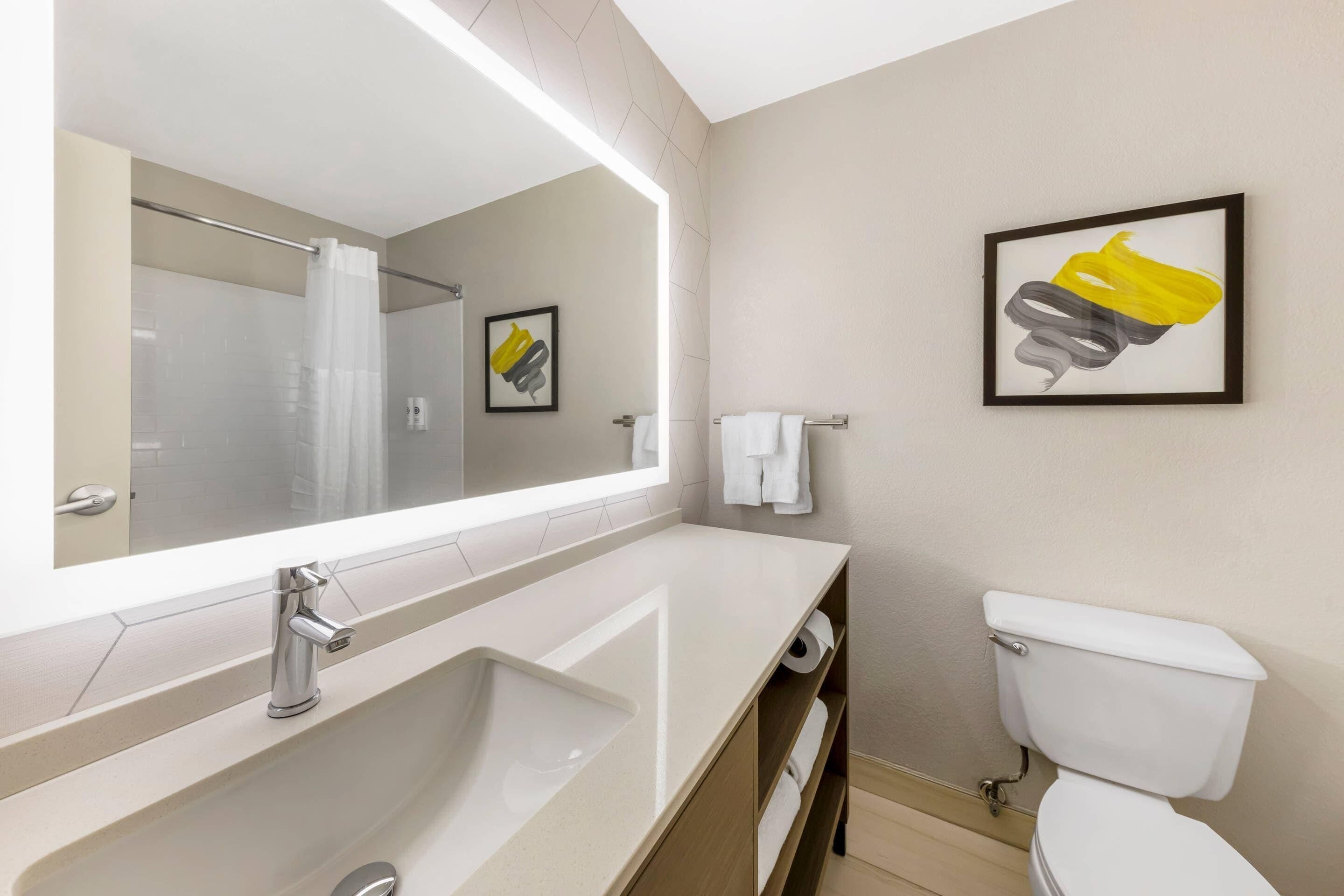 Un baño moderno con un espejo grande, un lavabo, un inodoro y una cortina de ducha.
