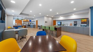 Un espace repas moderne avec une table en bois et des chaises colorées, une cuisine en arrière-plan et un comptoir doté d’un distributeur de boissons.