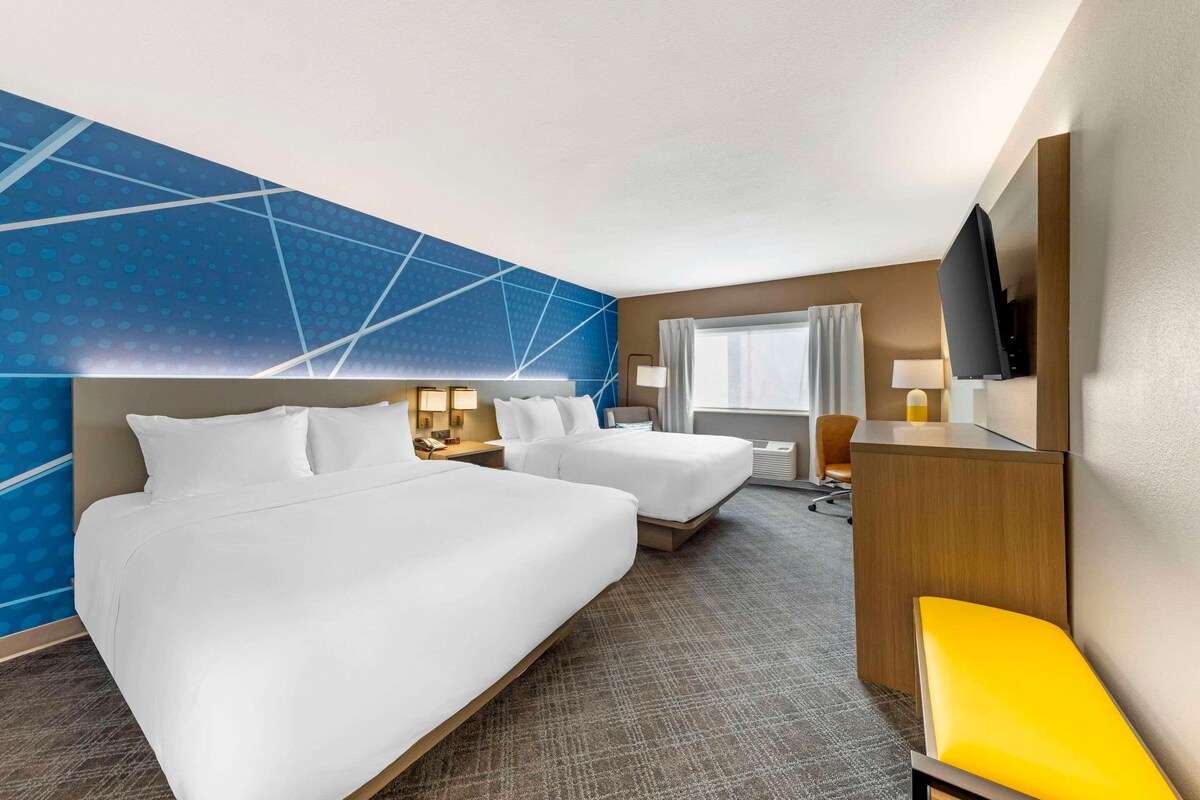 Habitación de hotel con dos camas, un escritorio, televisor y ventana con cortinas.