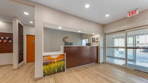 Un espace d’accueil comprenant un comptoir de réception en bois, une enseigne fixée au mur et une porte vitrée donnant sur l’extérieur.