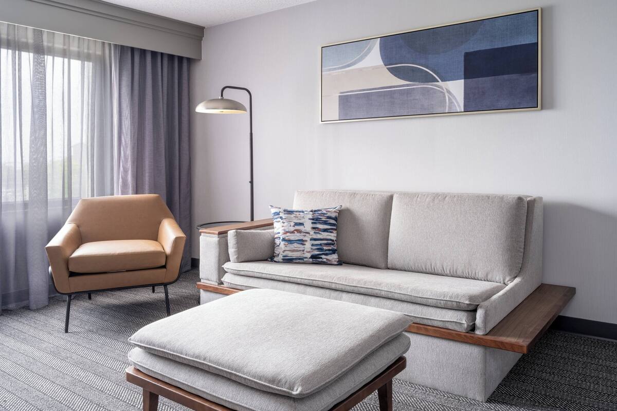 A modern hotel room with a sofa, armchair, and ottoman.