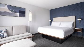 A modern hotel room with a large bed, a sofa, a floor lamp, and a wall-mounted lamp.