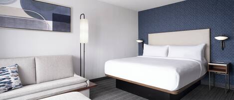 A modern hotel room with a large bed, a sofa, a floor lamp, and a wall-mounted lamp.