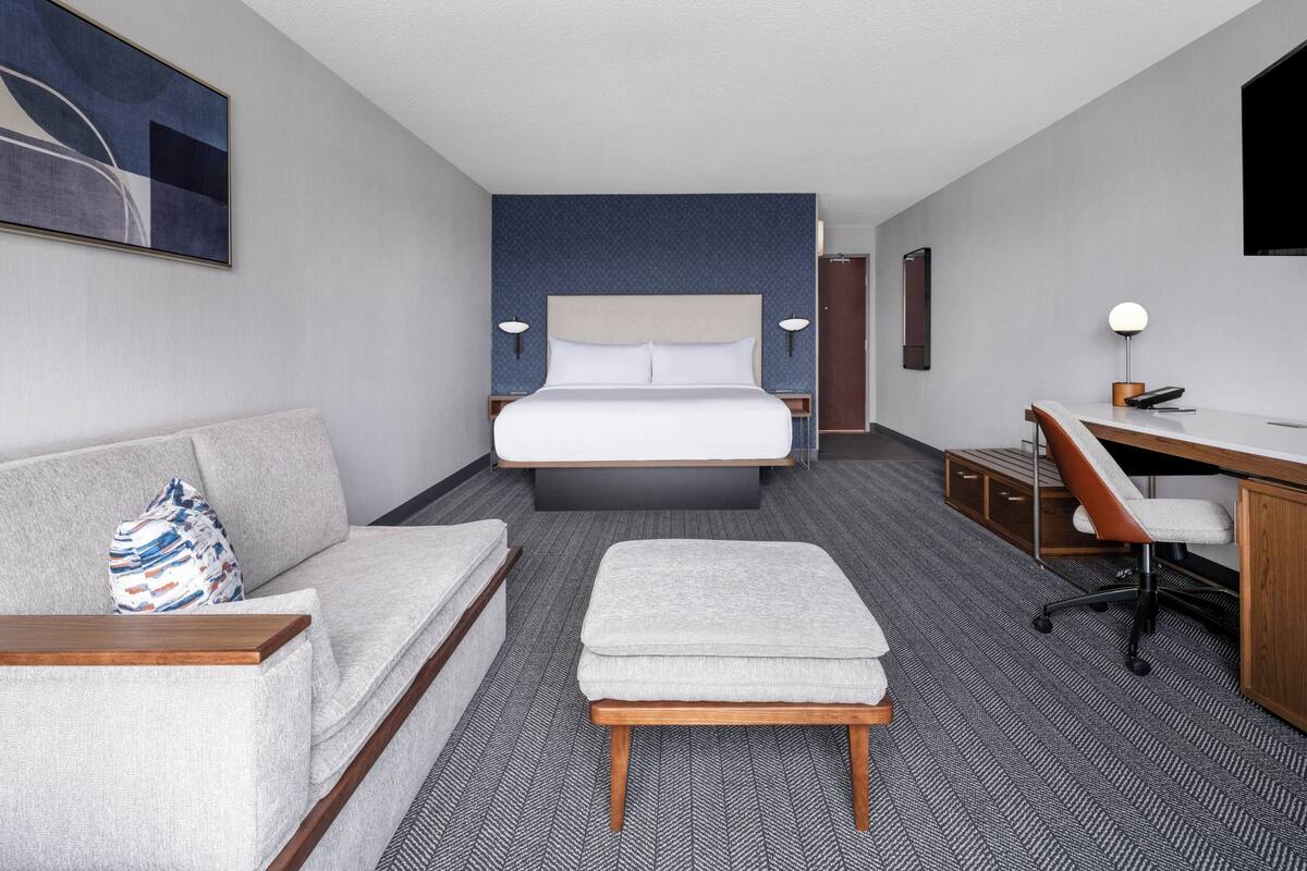 A hotel room with a bed, a sofa, a desk, and a chair.