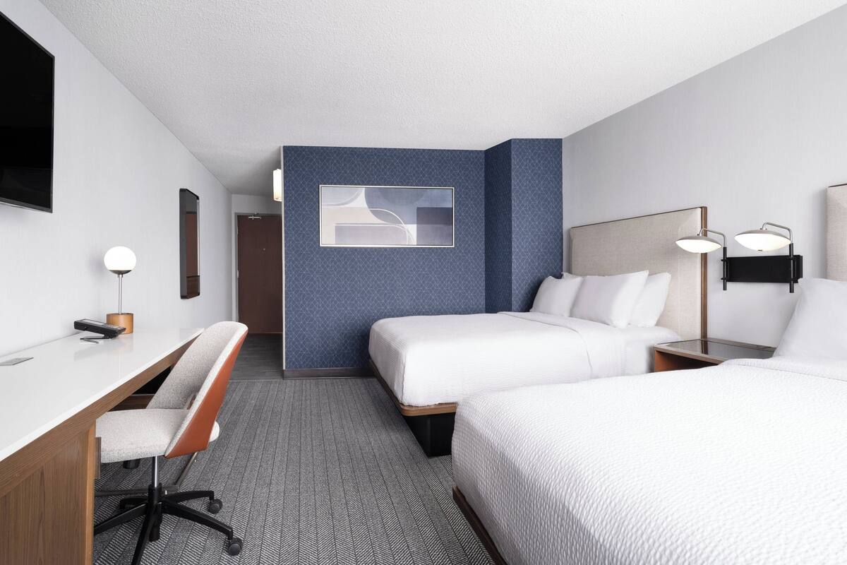A hotel room with two beds, a desk, and a chair.