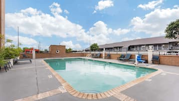A swimming pool with lounge chairs and a brick building in the background.