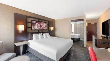 A hotel room with a large bed, a desk, a chair, a TV, and a bathroom visible through an open door.