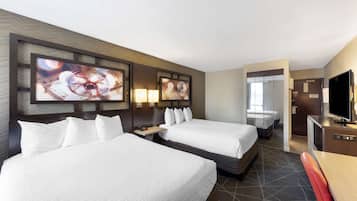 A hotel room with two beds, a desk, a TV, and artwork on the wall.