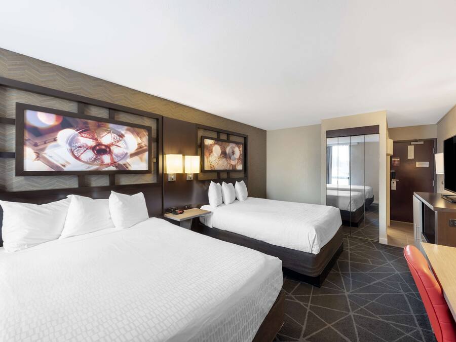 A hotel room with two beds, a desk, a TV, and artwork on the wall.