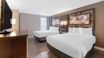 A hotel room with two beds, a desk with a TV, and artwork on the walls.