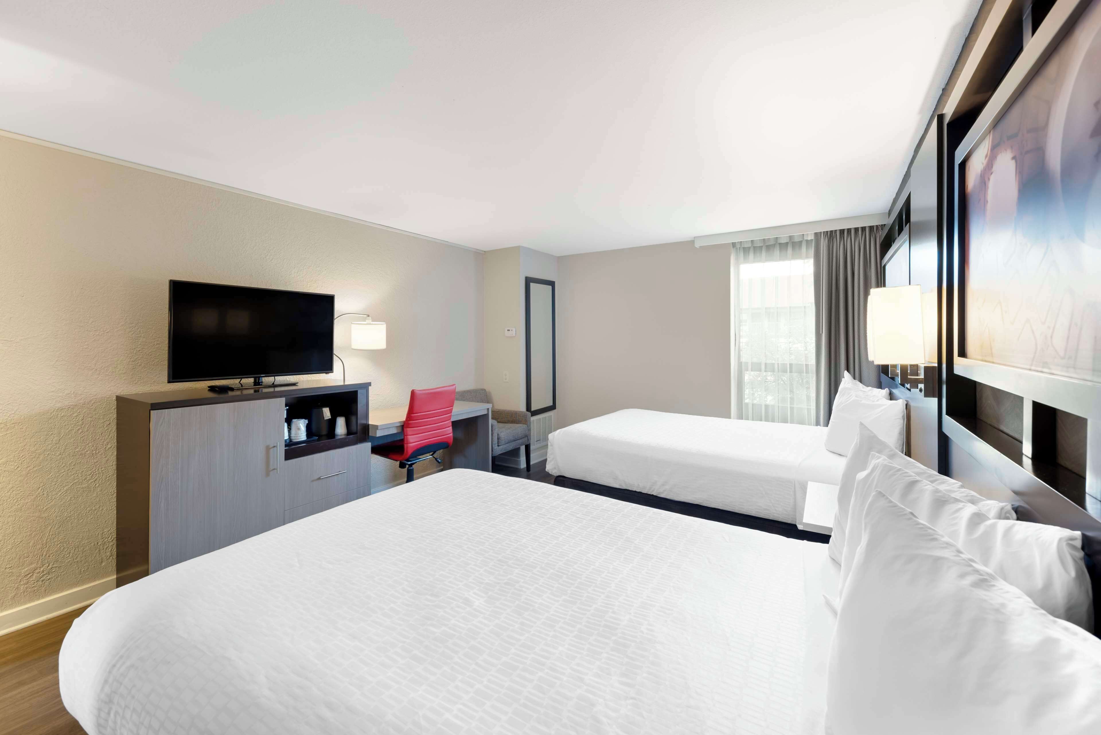 A hotel room with two beds, a desk with a chair, a television, and a window with curtains.