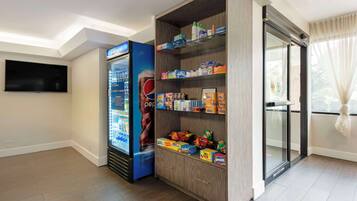 A hotel room with a minibar stocked with snacks, a refrigerator, and a flat-screen TV mounted on the wall.