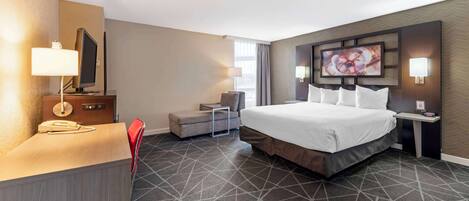 A hotel room with a large bed, a desk with a telephone, a chair, and a TV mounted on the wall.